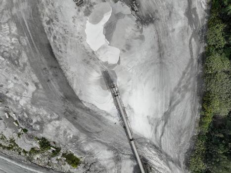 Industrial quarry crusher facility from above with conveyor belts and raw material piles, surrounded by erosion patterns and forest edge, symbolizing resource extraction and environmental pressure. photo