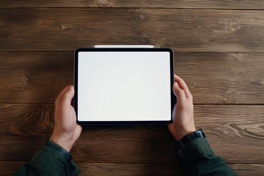 A person holding a tablet with a blank screen on a wooden table photo