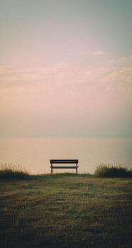 un banco sentado en un herboso campo con vista a el Oceano foto