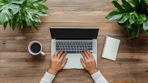Top view of hands typing on laptop on wooden table with coffee and plants photo