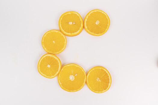 Bright orange slices are arranged neatly in a circular C shape on a white background flat lay. photo