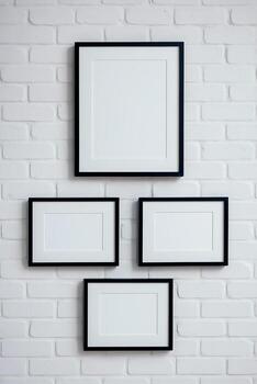 Minimalistic composition of four empty picture frames hanging on a white brick wall. Frames of different sizes. Universal image for layouts and design projects. photo