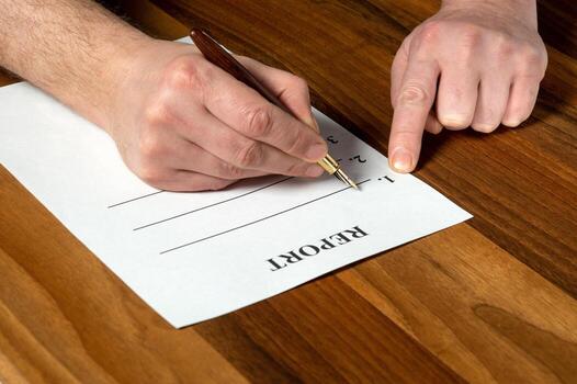 Drawing up report in a working environment on desktop. Close-up of man hands filling out blank with pen photo
