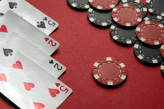 Four playing cards depicting a pair of twos and a pair of fives lie next to a stack of red and black chips on a bright red table, creating an inviting atmosphere for poker lovers photo