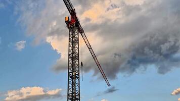 This showcases a construction crane against dynamic skies, transitioning from clouds to a stunning sunset, highlighting its structure and purpose video