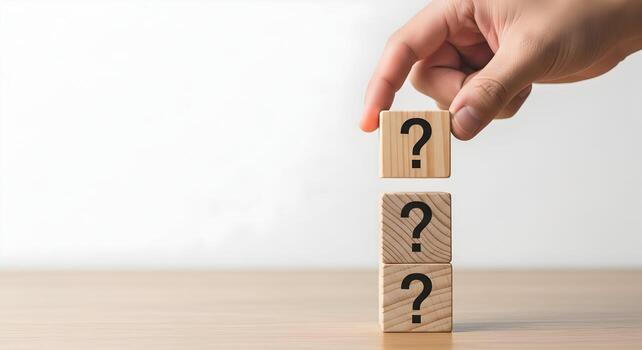 Hand placing wooden cube with question mark on a stack of similar blocks on a table, uncertainty concept photo