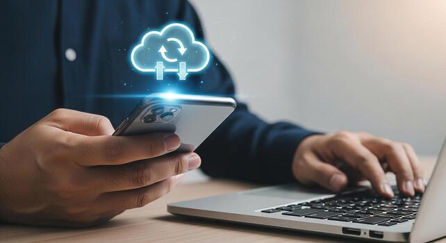 Person using smartphone and laptop to access cloud data showcasing seamless mobile cloud computing and data synchronization in a modern workspace The image conveys efficiency connectivity and technolo photo