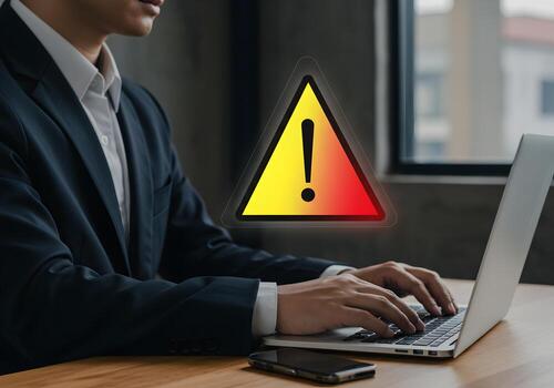 Businessman working on laptop with warning alert sign experiencing a problem or system error at his modern office desk Cybersecurity data breach and online threat concept image photo