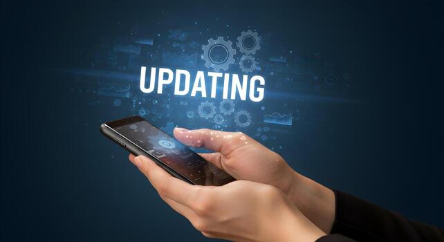 Person updating software on smartphone digital technology concept Closeup of hands holding phone with digital interface showing the word UPDATING with gears and charts in a dark blue background Modern photo