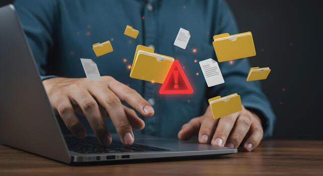 Person experiencing a critical data loss while working on a laptop files flying away with a warning sign signifying a corrupted system or accidental deletion photo