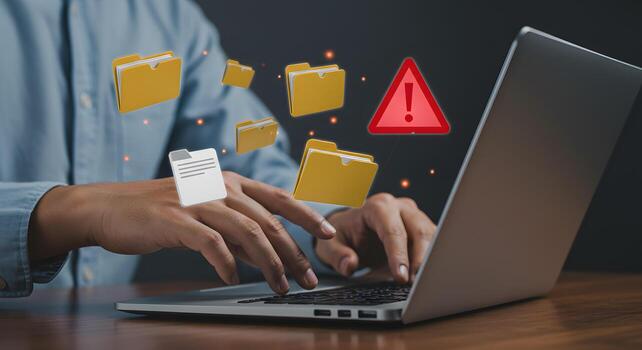 Person working on laptop computer troubleshooting a critical file access error digital data files and folders floating around the screen urgent alert warning sign photo