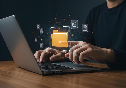 Person managing digital files and folders using a laptop computer at a wooden desk in a modern office showcasing efficient data organization and digital workflow photo