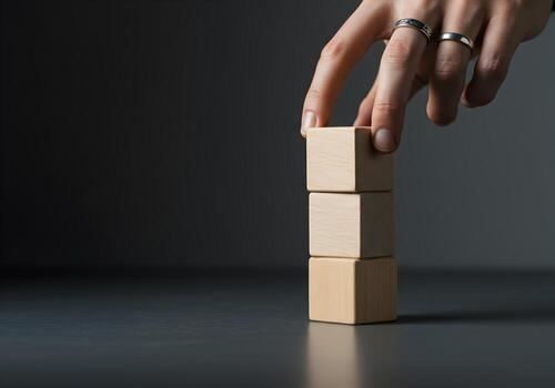 Hand placing wooden block on a stack building a tower on dark background concept of growth planning and strategy Image depicts business success development and achieving goals photo