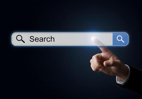 Hand using index finger to touch a glowing search bar with a magnifying glass icon on a dark background representing the concept of digital search and exploration This image is perfect for illustratin photo