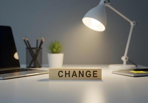 Wooden block with the word CHANGE on a modern office desk illuminated by a desk lamp signifying transformation and new beginnings photo