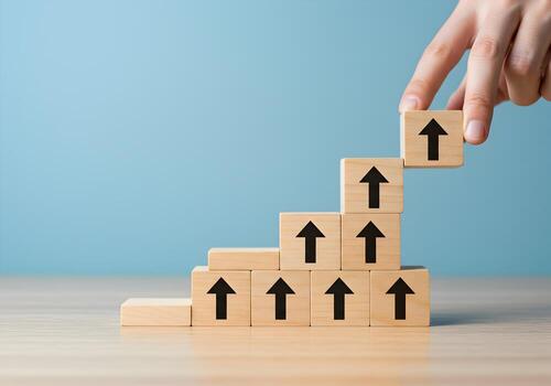 Hand placing wooden block with upward arrow on top of a growing stack of similar blocks on a desk symbolizing growth progress and reaching goals photo