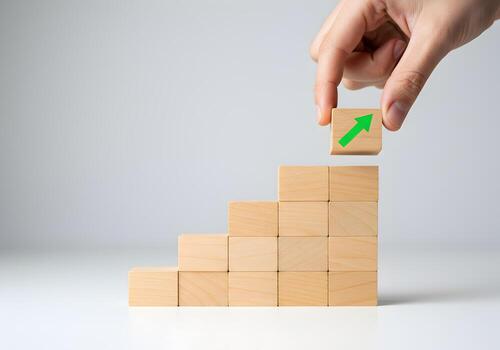 Hand placing wooden block with green upward arrow on top of a growing stack of blocks symbolizing growth progress and success The image represents concepts of development achievement and strategic pla photo