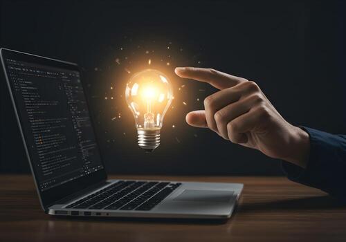 Hand pointing at glowing lightbulb above laptop screen displaying code symbolizing innovative software solution digital workspace concept photo