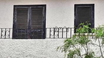The features a charming white building with black shutters and a balcony with wrought iron railing, enhanced by a tree, blending nature and architecture video