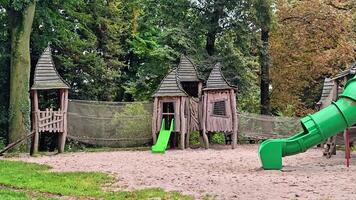 en vibrerande lekplats centrum på en stor grön glida, var barn glatt klättra och glida, omgiven förbi färgrik strukturer och gräs- områden video