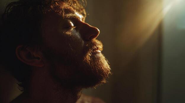 A man is bathed in sunlight with his eyes closed, in a moment of reflection. photo