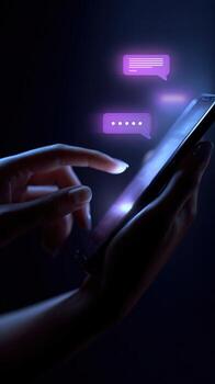 Person using a mobile device with two neon purple chat bubbles above the phone screen in the dark photo