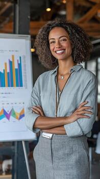 Smiling woman with crossed arms stands before a chart in an office environment during a presentation photo