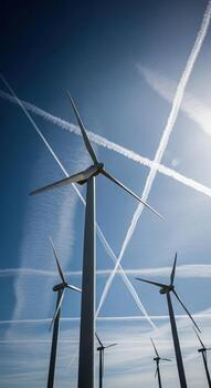 Wind turbines reaching for the sky with contrails forming patterns in the bright blue atmosphere photo