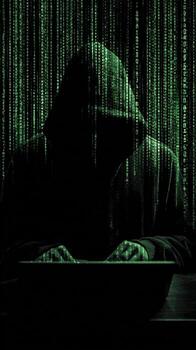 Person in a hoodie typing on a laptop with a green digital rain style background behind them photo