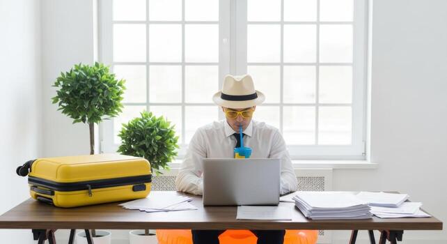 Man with hat at desk with laptop suitcase and drink in office space near plants and window photo