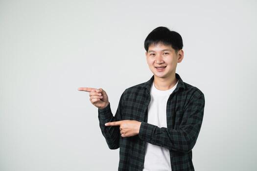 Friendly young man in casual outfit points with both hands to the side against a plain white background, expressing enthusiasm and positivity in a studio setting photo