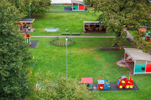 Colorful playground featuring a toy train, slides, fenced sandbox, and covered seating, surrounded by trees and pathways in a grassy park. photo