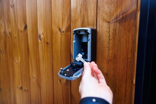 un mano en un oscuro manga recupera un llave desde un abierto pared montado caja de seguridad. el pulido de madera superficie muestra visible grano patrones, agregando textura. foto