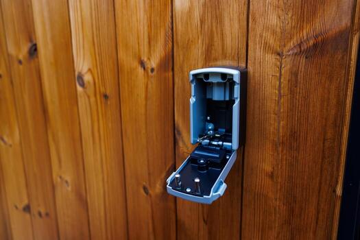 An open metallic lockbox reveals its internal mechanism, including a keypad, set against a wooden surface with a distinct grain pattern. photo