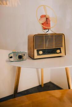 Vintage technology featuring radio, camera, and fan arranged on small white table, creating nostalgic atmosphere that transports viewers back to simpler times. Vintage technology, retro radio, camera photo