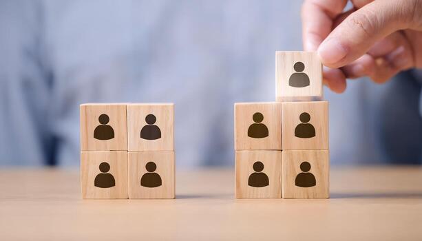 Hand placing wooden block with person icon on top of other blocks, symbolizing team building, human resources, or leadership. photo