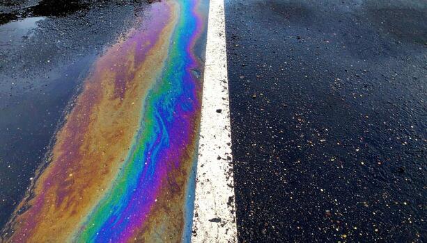 Parking lot oil film rainbow in a narrow strip on dark asphalt top copy area representing iridescent surface suitable for automotive editorial and abstract design photo