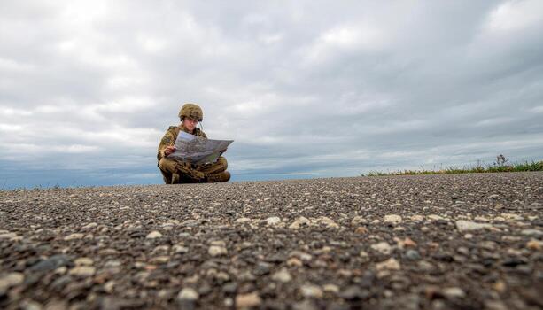 Fictional soldier reading paper map under overcast sky gentle top light neutral gear with covered badges wide negative space field navigation and planning concept photo