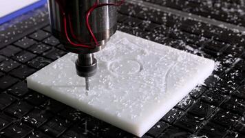 A CNC router machine working on a white plastic block, engraving a pattern with high precision in close-up video