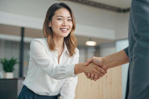 Asian woman real estate agent shakes hands with a man in a business setting she is smiling and she is happy. Contract signing concept photo