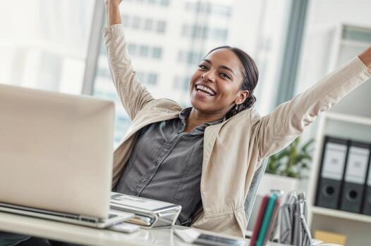 A woman is smiling and laughing while sitting at a desk with a computer, she is wearing a business suit and she is happy and excited rejoicing success photo