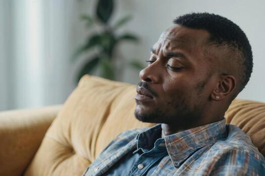 Face of African American man sits on a sofa with a serious expression, family problems. Relationship difficulties concept photo