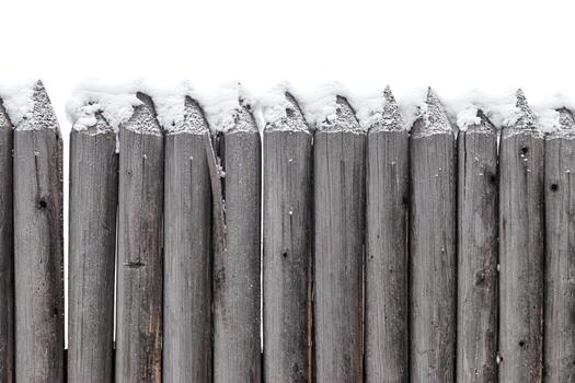 Close up of wooden fence with pointed tops covered snow in winter season, old rustic border against white background. Vertical wood palisade with round tree sharp logs, timber textured wall. photo