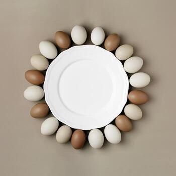 Top view of chicken eggs around white empty plate as copy space. Food round frame for national eggs day. Minimal style natural brown eggs on colored background. Monochrome gradient brown photo