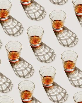 Crystal Whiskey Glasses a t sunlight, repeated pattern on beige background, minimal neutral layout, aesthetic top view summer still life, refraction at shine alcohol drink, dark shadow, caustics photo