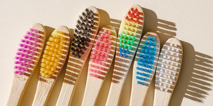 Eco friendly textured Bamboo toothbrushes in row with colored bristles at sunlight on beige background. Sustainable living concepts, minimal style aesthetic banner, top view set wooden brushes photo