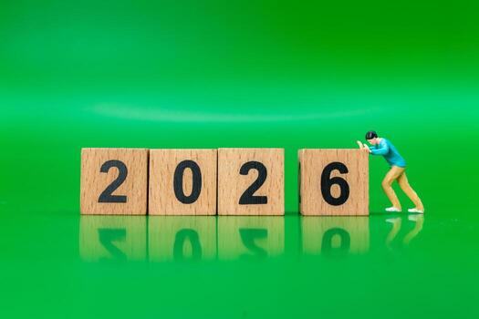 Miniature Figure Pushing Wooden Blocks to Form 2026 on Green Background photo