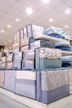 Stack of neatly packaged bedding sets in various colors and patterns displayed in a retail store, showcasing modern textile design and organization for home decor photo