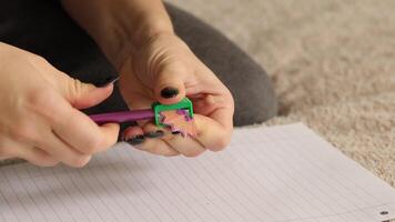 en person demonstrerar skärpning en lila penna använder sig av en grön pennvässare på en ark av papper. de fokus är på de propert resultat av detta grundläggande skrivning verktyg video