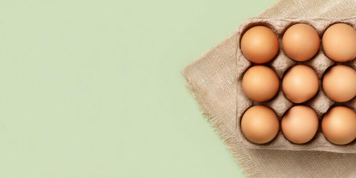 Flat lay of fresh farm eggs in recyclable carton on rustic fabric background photo